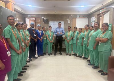 Group of healthcare workers in green scrubs posing for a photo in a hospital corridor, with a man in a blue shirt at the center.