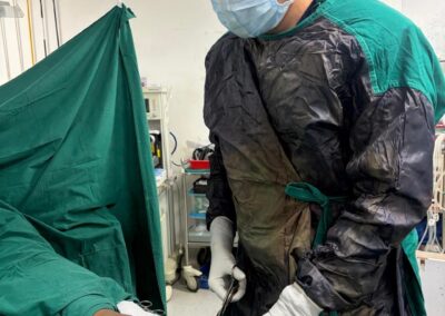 Surgeon in a gown, mask, and cap applies sterile dressings to a patient’s forearm during surgery.